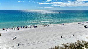 A beach with white sand, clear blue water, and a few umbrellas.