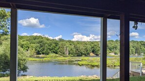 Une vue depuis une véranda donnant sur un lac, lui-même entouré d’une végétation luxuriante.