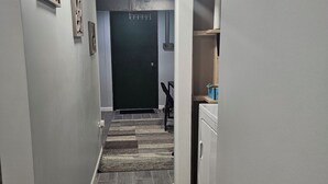 Un couloir avec un tapis à motifs, une porte noire et un appareil électroménager blanc, probablement un lave-linge et un sèche-linge.
