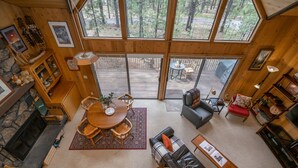 A spacious living area with a fireplace, wooden furniture, and large windows offering a view of the outdoors. - Mink #8 Close to SHARC and 8 SHARC Passes! Close to Village! (Sunriver)