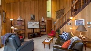 A cozy room with wooden walls, a staircase, a sofa, a coffee table, and a sign reading "Sunset Lodging." - Mink #8 Close to SHARC and 8 SHARC Passes! Close to Village! (Sunriver)