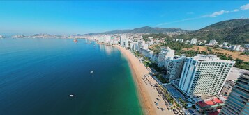 Un paisaje costero con playa, edificios de gran altura y una montaña al fondo.