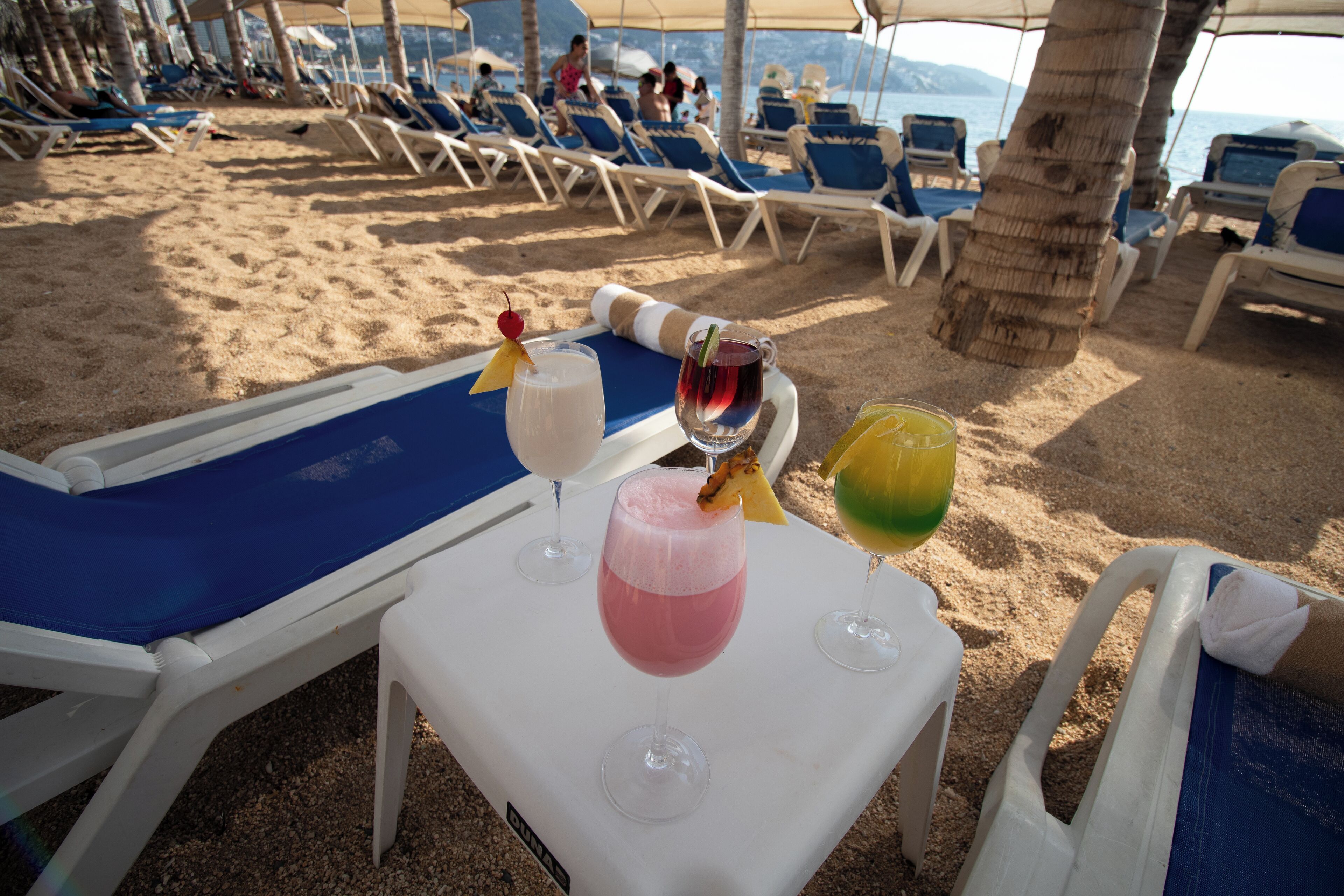 Un área de descanso en la playa con tumbonas, una mesa con bebidas y vistas al mar.