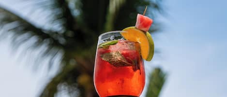 A glass of red beverage with a slice of lime and a strawberry on a table with a palm tree in the background.