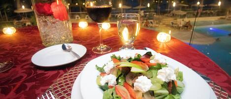 A dining table with a salad, wine glasses, and a candle.