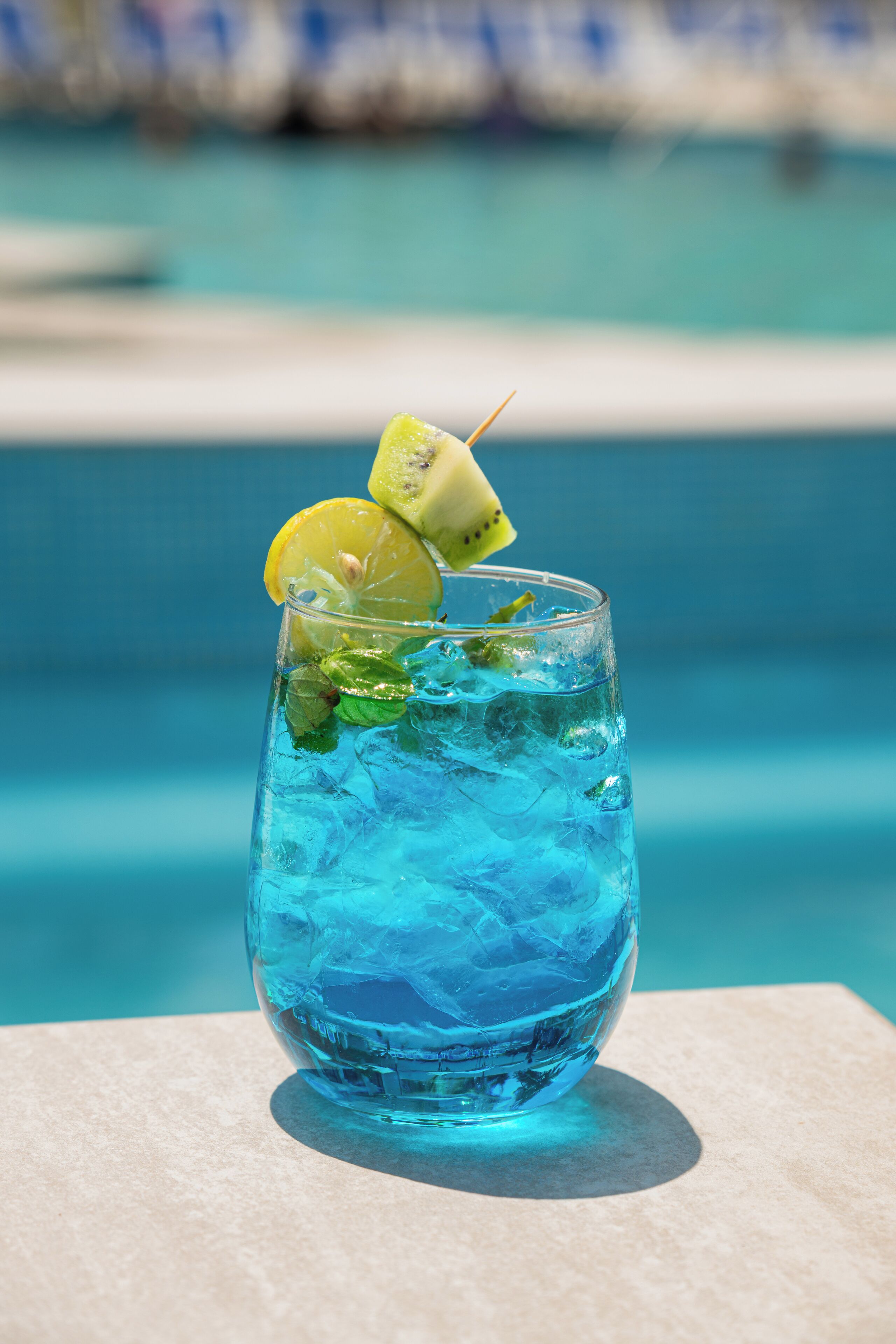 Ein Glas blaues Getränk mit Limette und Minze, platziert an einem Tisch am Pool.