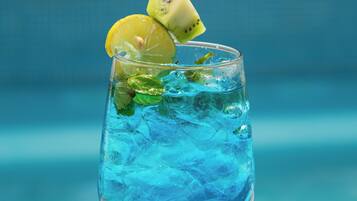 Ein Glas blaues Getränk mit Limette und Minze, platziert an einem Tisch am Pool.