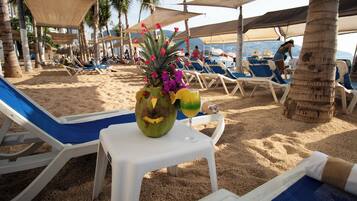 Una playa con tumbonas, una mesa con un coco y flores, y palmeras.