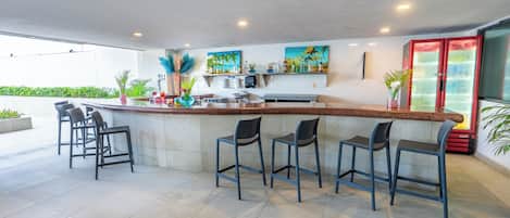 A modern bar area with a long counter, multiple bar stools, and a refrigerator.