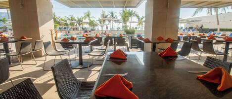 Un restaurante con terraza, mesas, sillas y sombrillas, con vistas a una piscina.