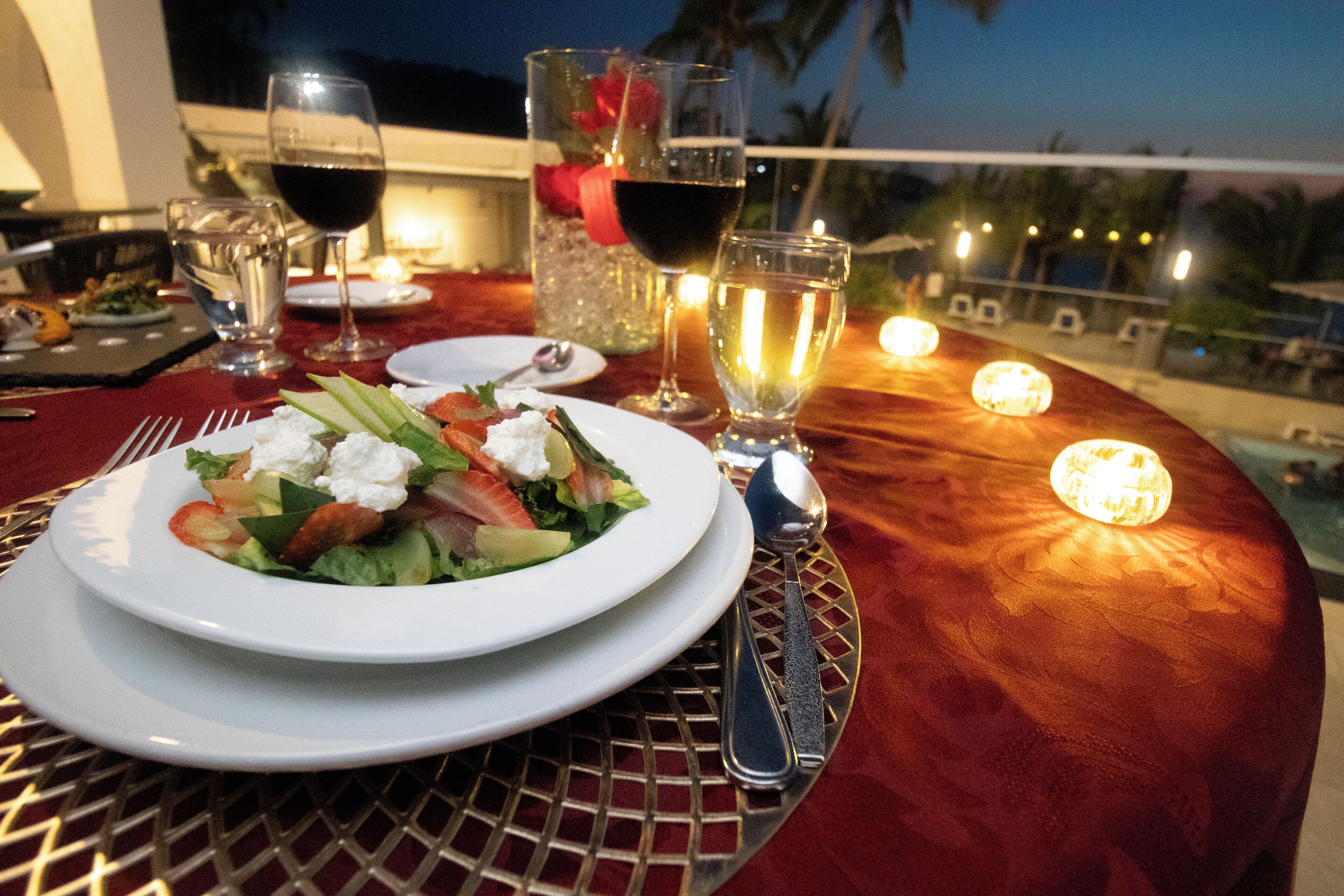 Una mesa servida para una comida, con una ensalada, copas de vino y una vela.