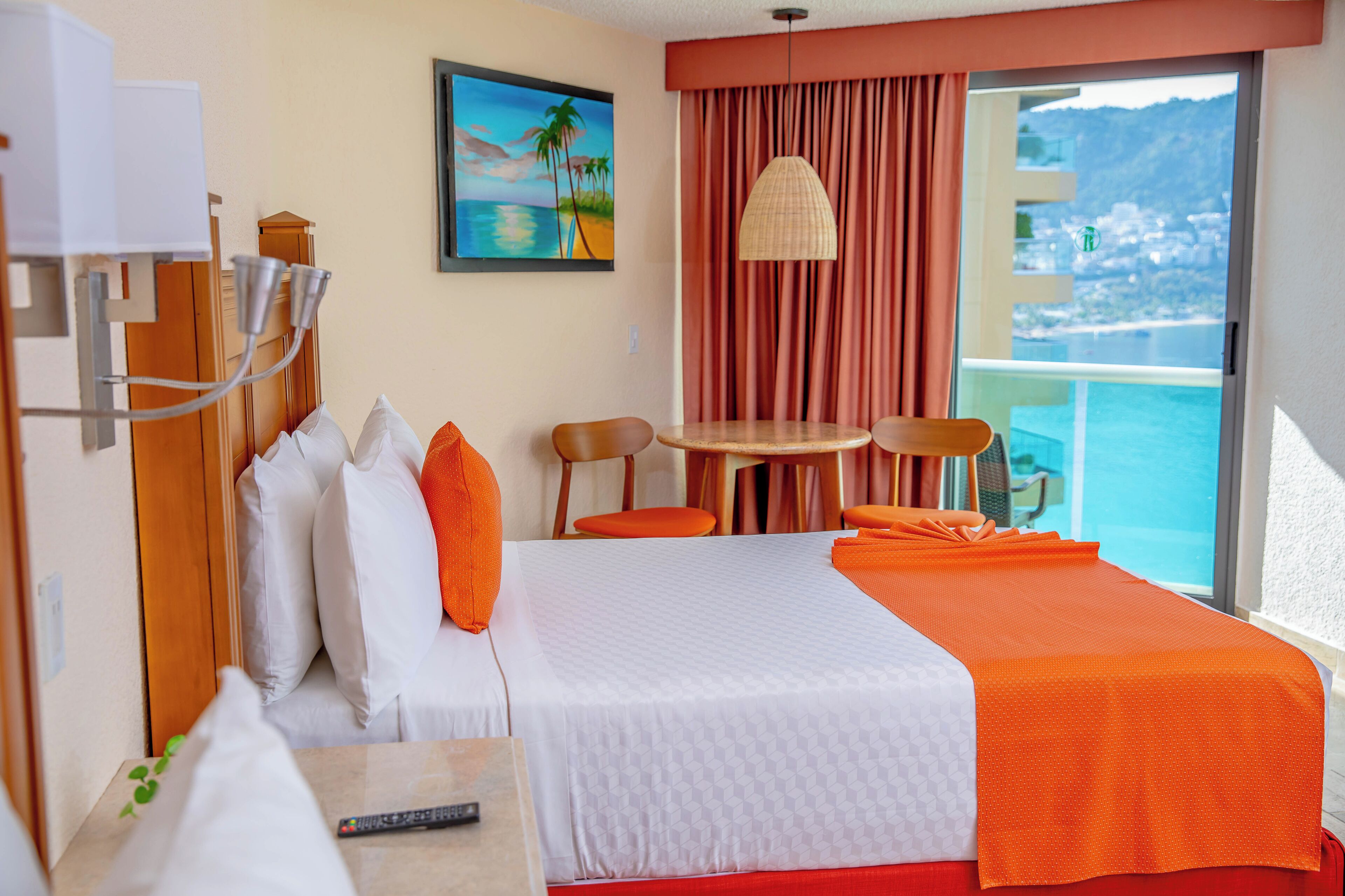 Habitación de hotel con cama, escritorio, silla, mesa, un cuadro y vista al mar.