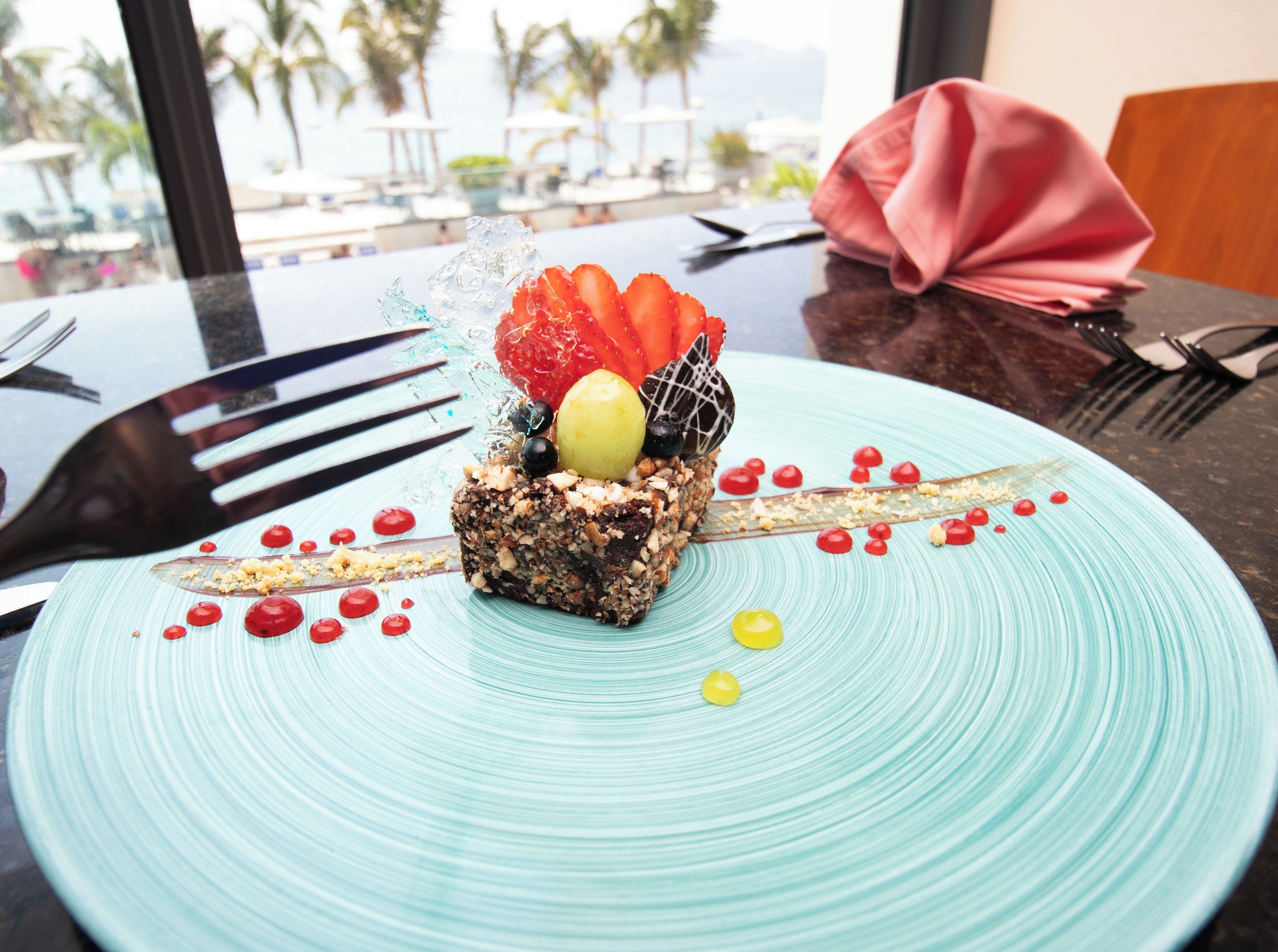Un postre en un plato con vistas a palmeras y una piscina al fondo.
