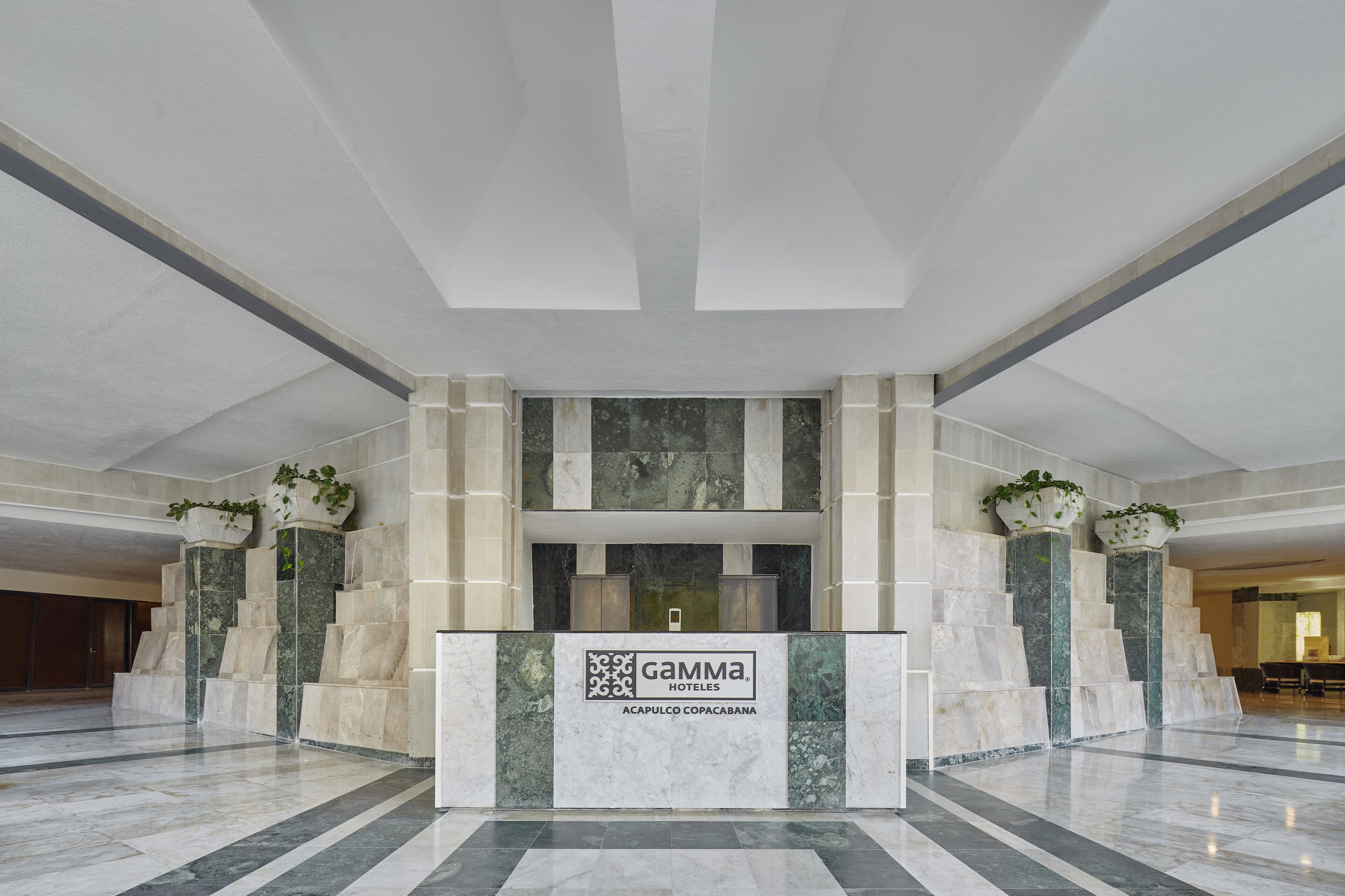 Een receptiebalie van een hotel met een marmeren vloer, een incheckbalie en het logo van Gamma Hotels.