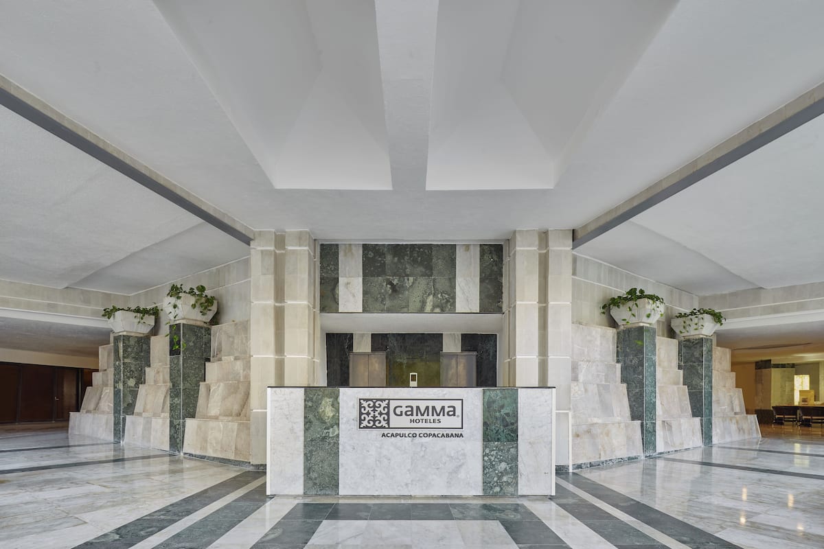 Un comptoir d’accueil d’hôtel avec un sol en marbre, un guichet d’enregistrement et le logo de la chaîne Gamma Hotels.