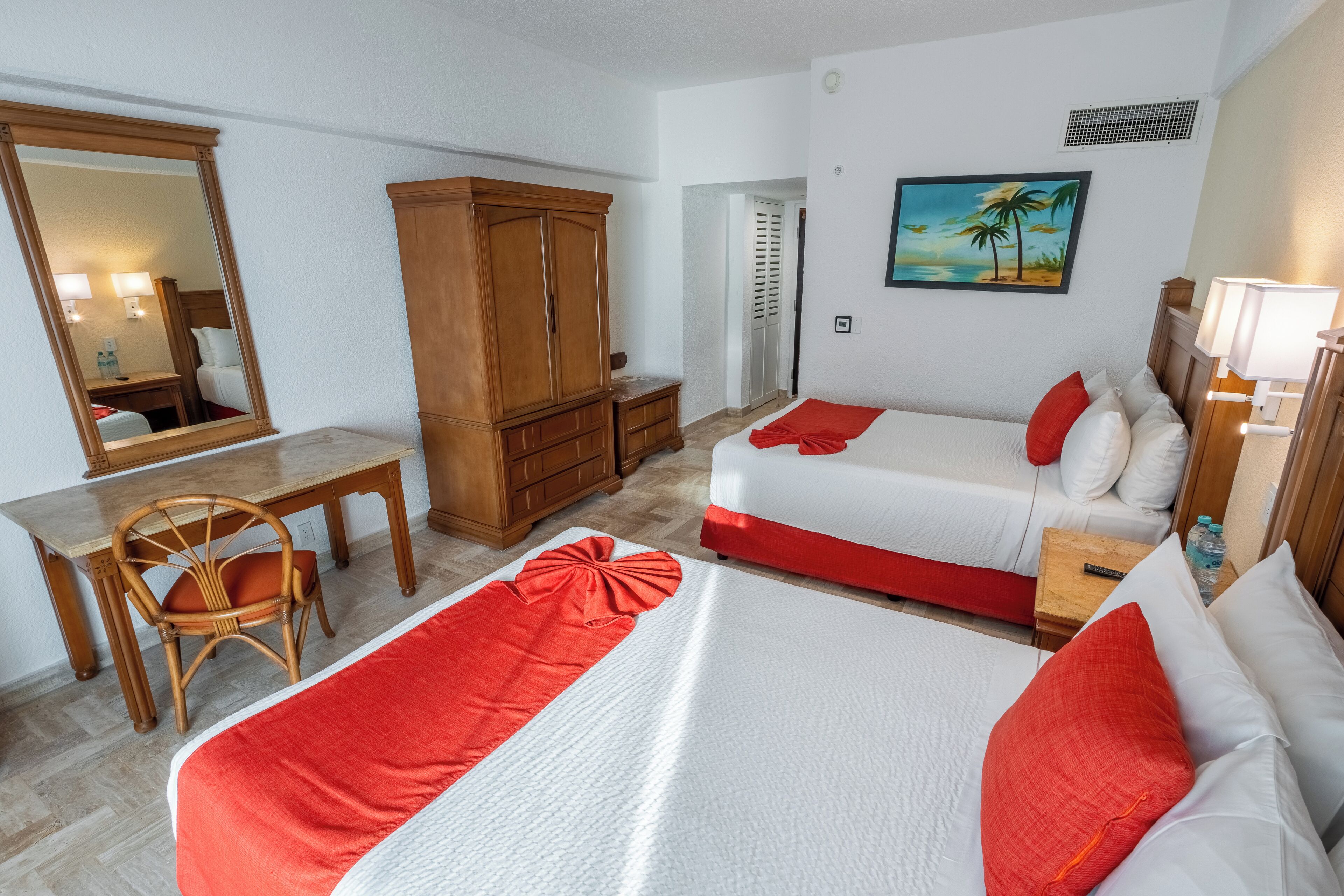 A hotel room with two beds, a desk, a chair, a wardrobe, and a painting of a beach scene.