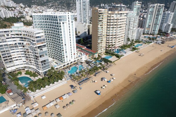Un hôtel de grande hauteur doté de nombreux balcons, d’une piscine et d’un espace de plage avec des parasols.