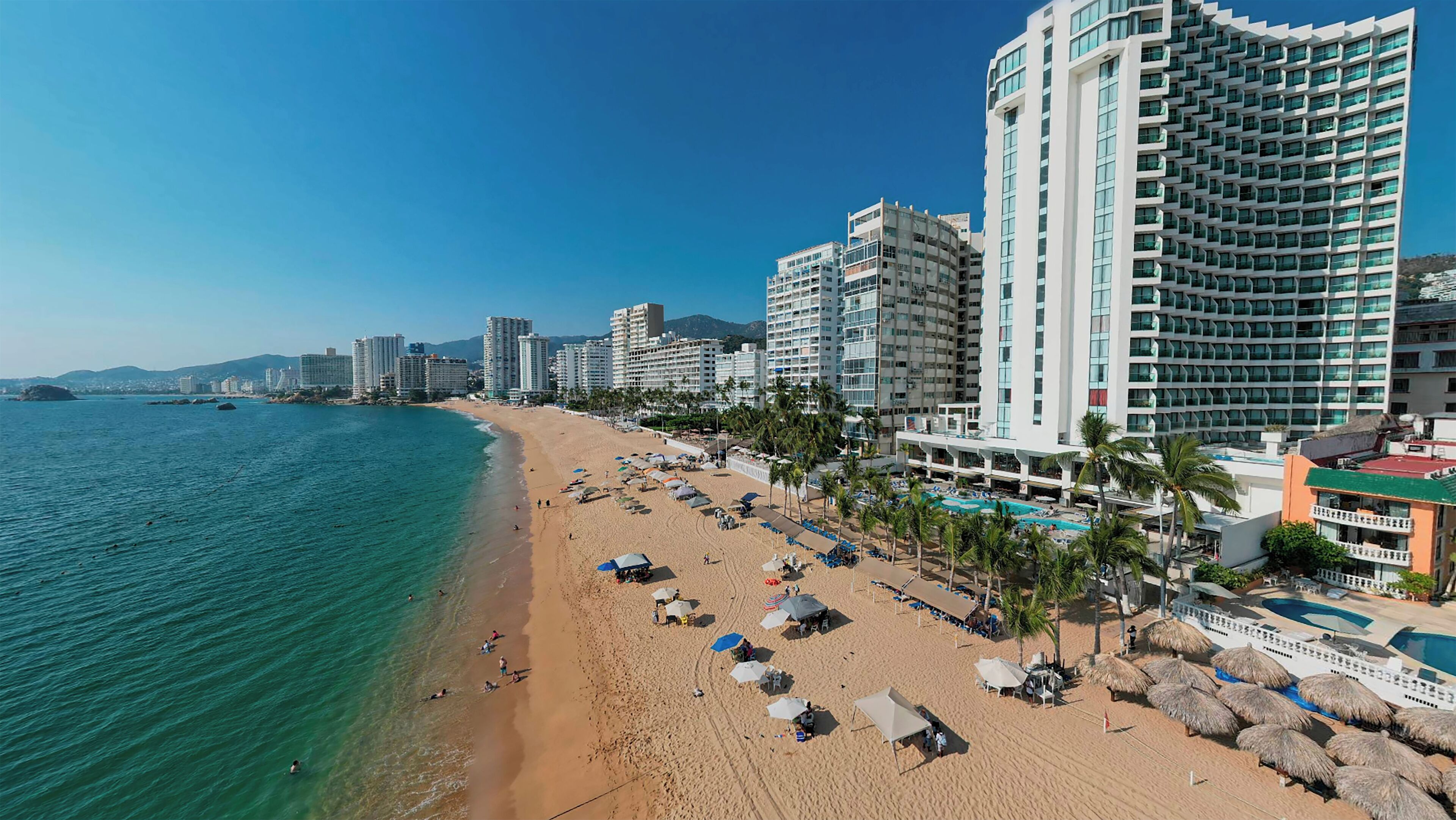 A beach with a hotel and a pool area.
