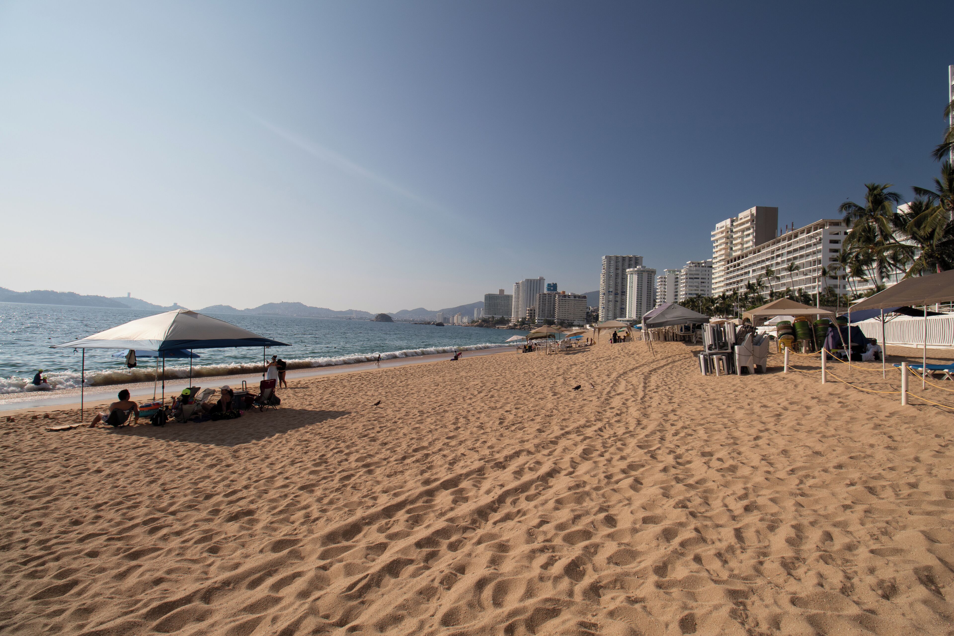 A beach with umbrellas, a sandy shore, and buildings in the background.