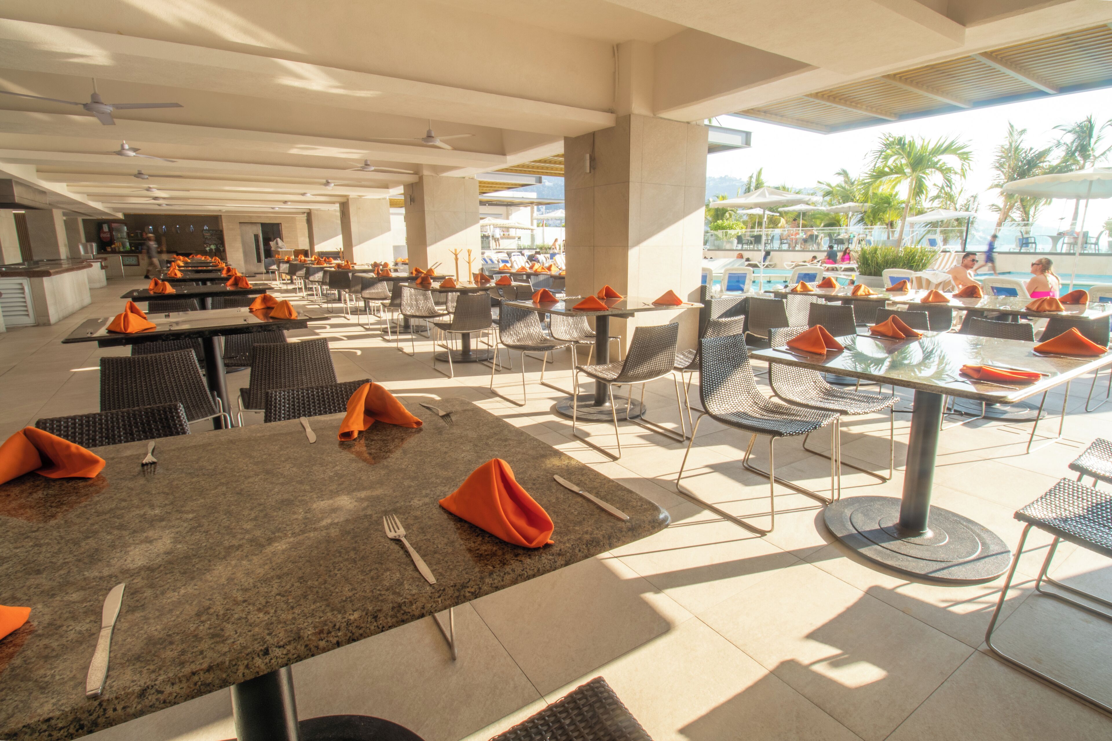 An outdoor dining area with tables and chairs, a pool in the background, and a view of the resort.