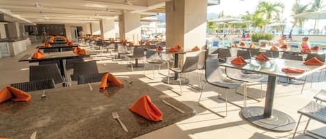 An outdoor dining area with tables and chairs, a pool in the background, and a view of the resort.