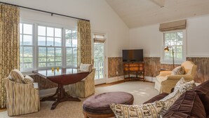 A spacious living room with a large window, a dining table, a sofa, and a television. - Ramsay Estate Carriage House – Luxury Retreat with Mountain Views (Greenwood)