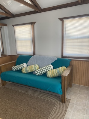 Un sofá azul aguamarina con cojines estampados, vigas de madera en el techo y ventanas con persianas.