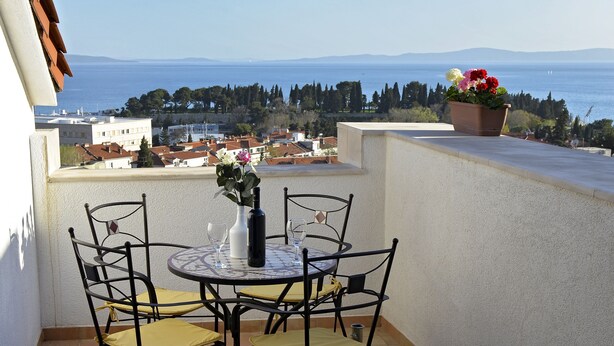 A terrace with a table and chairs, a potted plant, and a view of the sea and buildings. - Apartment FRANKA Split (Split)