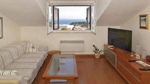 A living room with a sofa, a glass-top coffee table, a TV, and a window with a view of buildings and the sea. - Apartment FRANKA Split (Split)