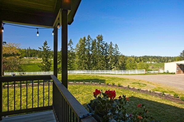 A covered outdoor area with a view of a fenced field and trees.