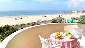 Een balkon met een tafel gedekt voor twee, met uitzicht op een strand en een heldere lucht.