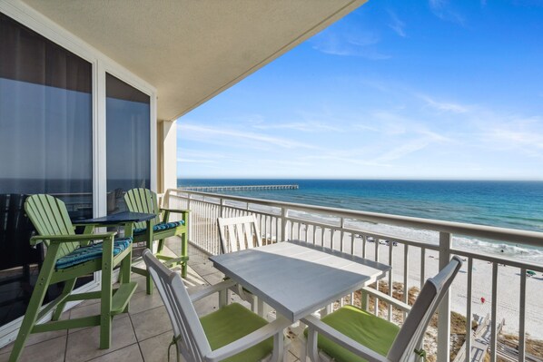 Un balcon avec une table et des chaises, donnant sur une plage et l’océan.