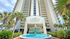 A high-rise hotel with a central fountain, palm trees, and a clear sky.