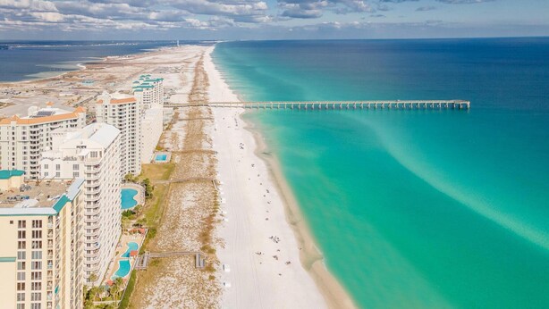 A coastal hotel with multiple buildings, a beach, and a pier extending into the ocean.