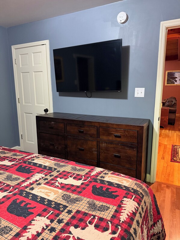 A bedroom with a bed, dresser, TV, and a door.