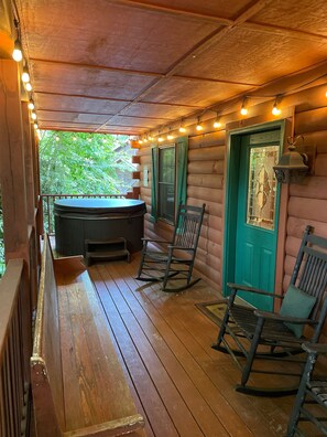 A wooden deck with a hot tub, rocking chairs, and string lights.