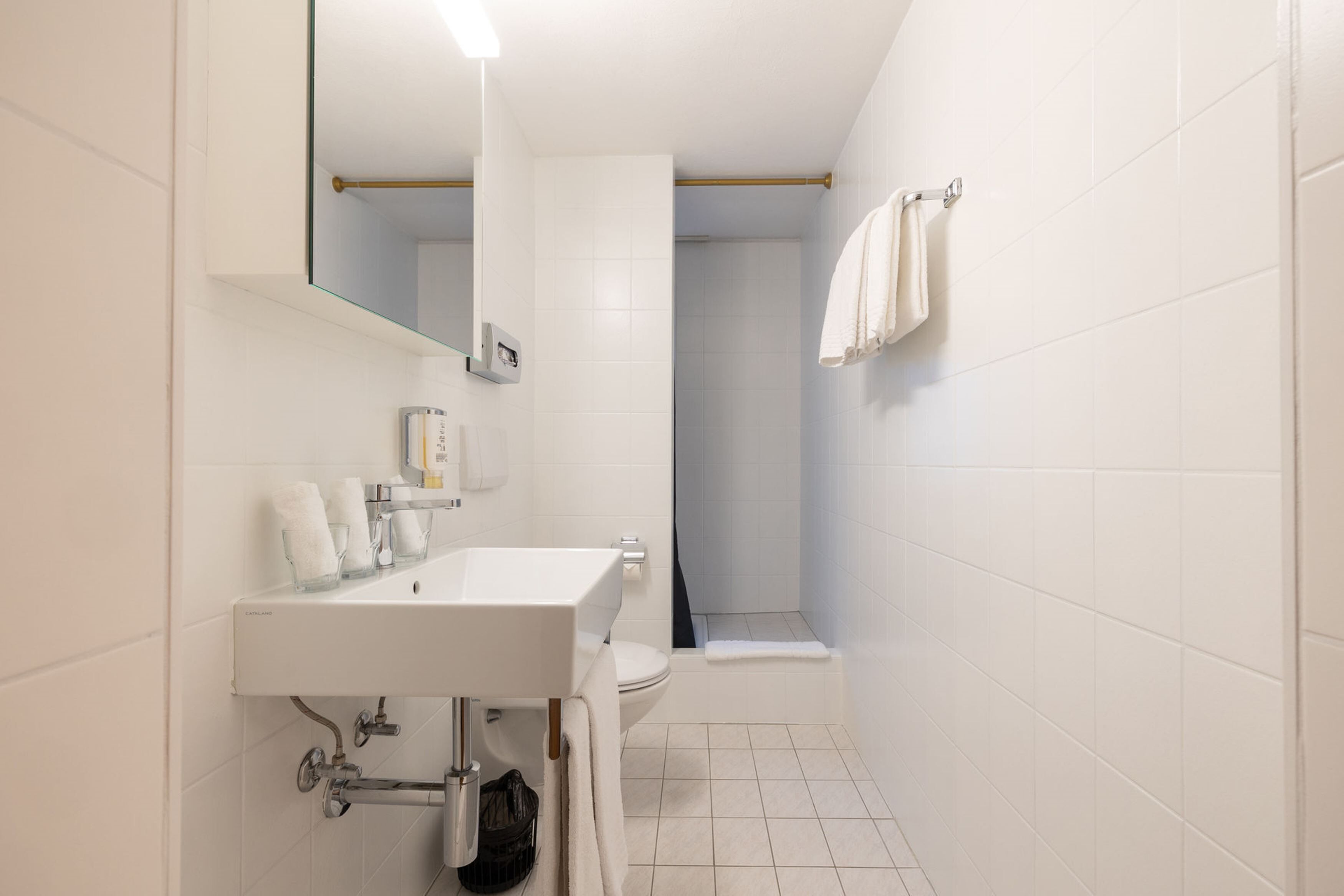 Moderni kylpyhuone, jossa on valkoinen pesuallas, peili ja wc-istuin.
