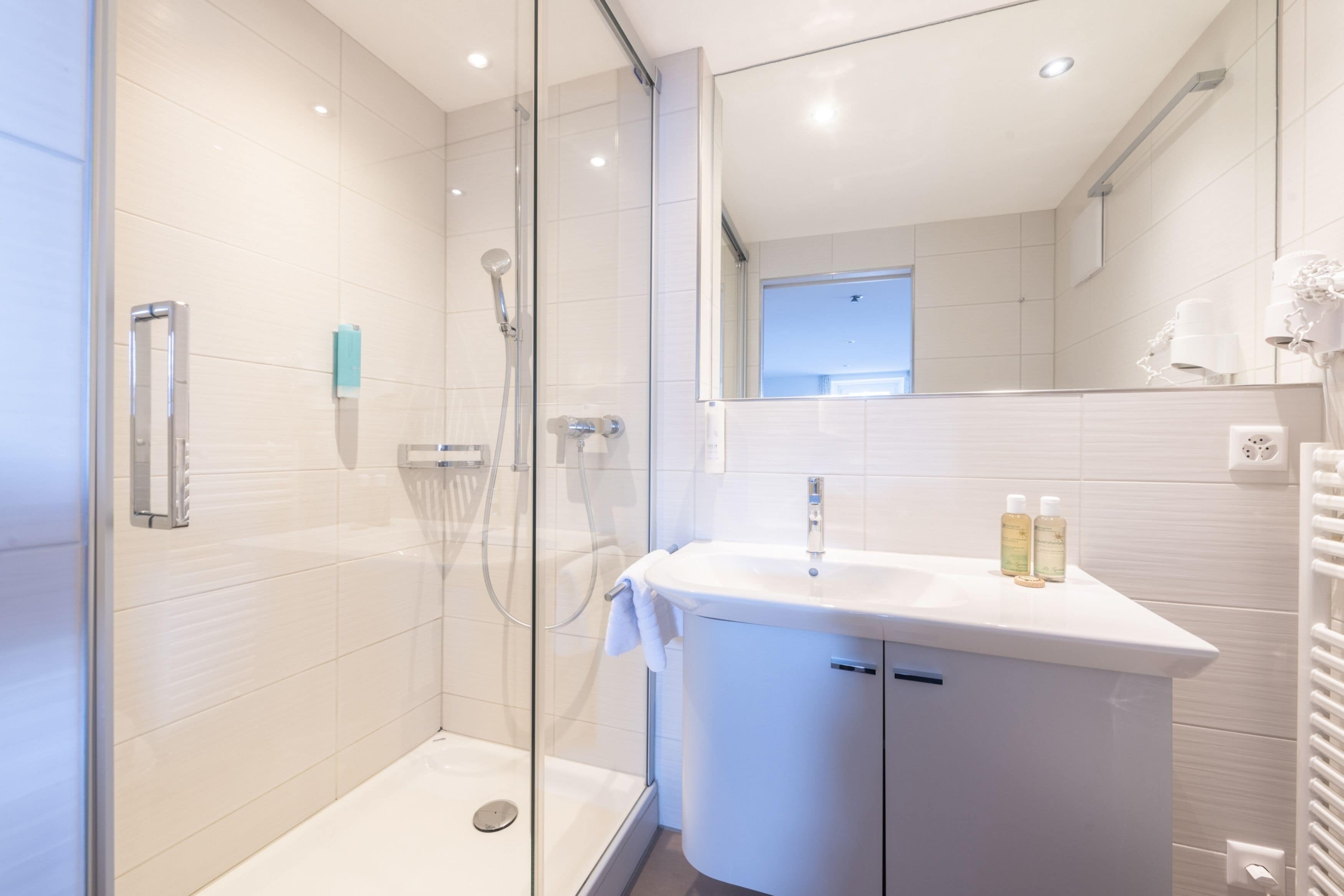 A modern bathroom with a glass-enclosed shower, a white sink with toiletries, and a large mirror.