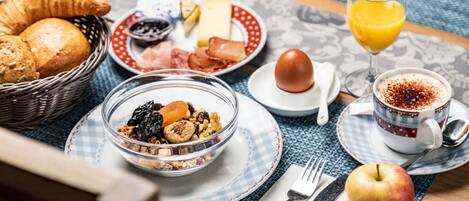 Desayuno con cruasanes, un tazón de cereal, un vaso de jugo de naranja, una taza de café y una manzana sobre una mesa.