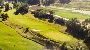 Een golfbaan met glooiende heuvels, bomen en een heldere lucht.