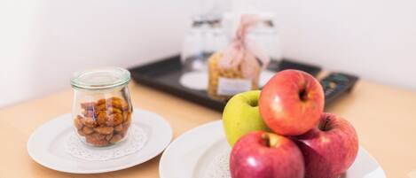 Una mesa con un tarro de cristal con nueces, un plato con tres manzanas y una pequeña botella con un lazo rosa.