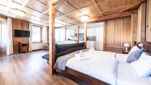 Een slaapkamer met houten lambrisering, een groot bed, een televisie en uitzicht op de keuken.