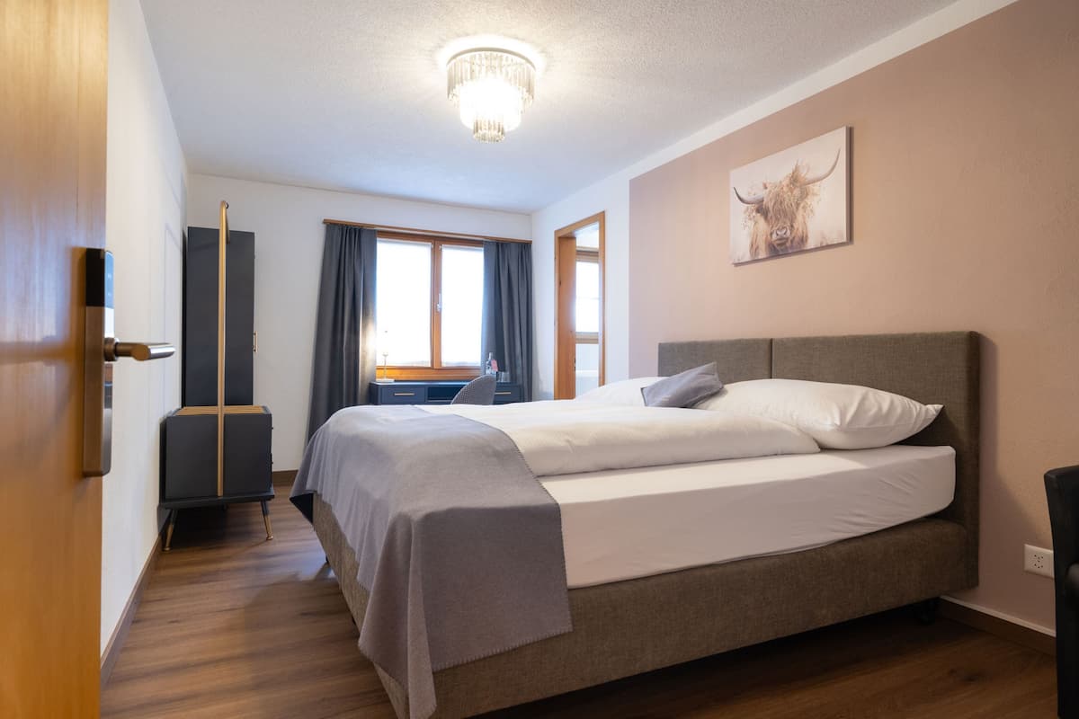 Hotellihuone, jossa on suuri sänky, työpöytä, tuoli ja ikkuna, jossa on verhot.