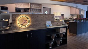 Een moderne bar met een houten toonbank, planken met glazen en een koffieapparaat.