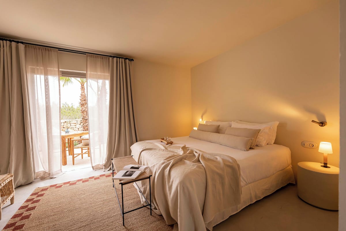 Une chambre à coucher comprenant un lit, une table de chevet, une lampe et donnant sur un patio avec une table et des chaises.