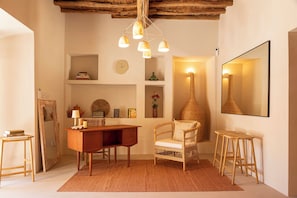 A cozy room with a wooden desk, a wicker chair, a mirror, and a hanging light fixture.