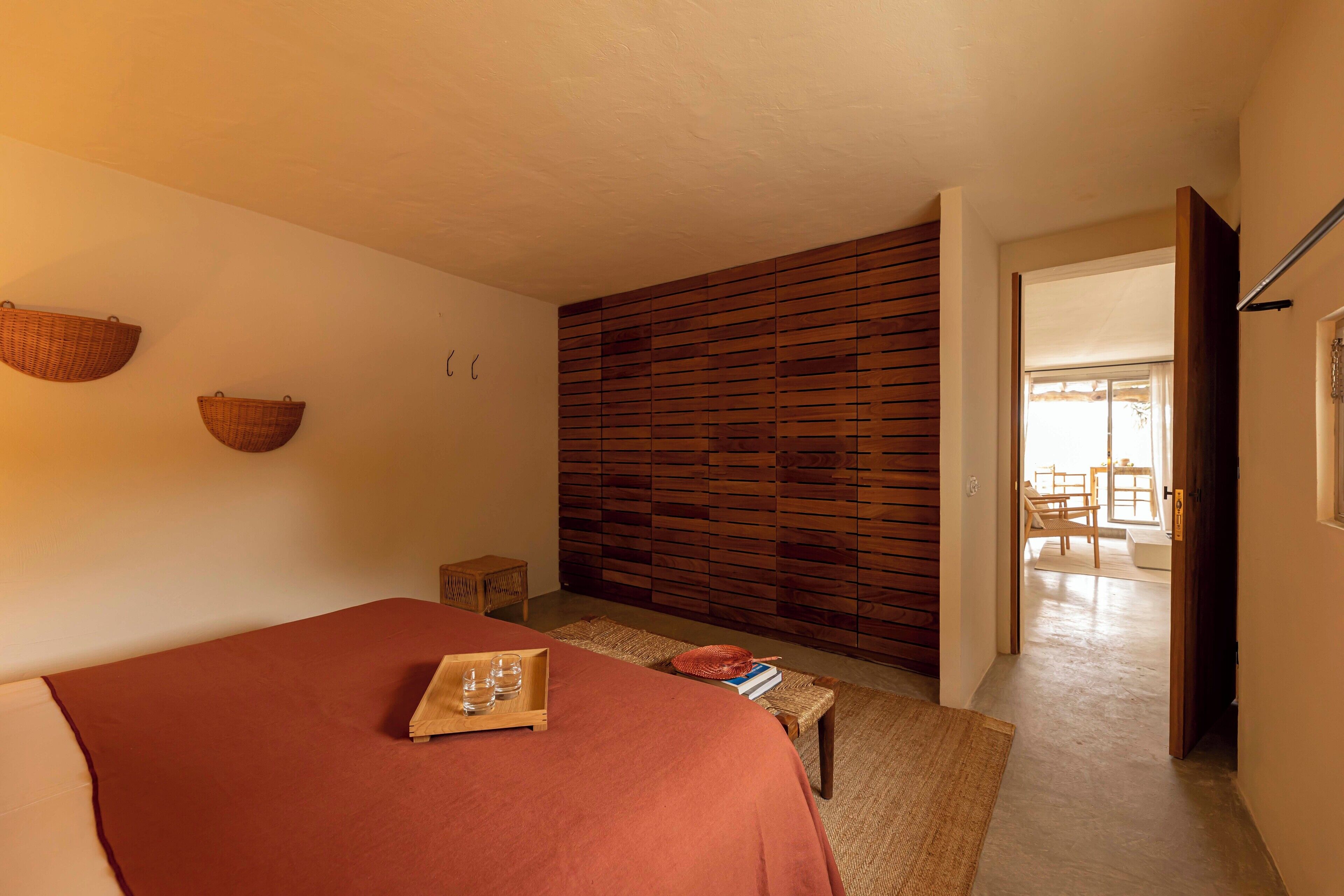 A bedroom with a bed, a wooden slat wall, a small table with a tray, and a doorway leading to another room.