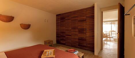 A bedroom with a bed, a wooden slat wall, a small table with a tray, and a doorway leading to another room.