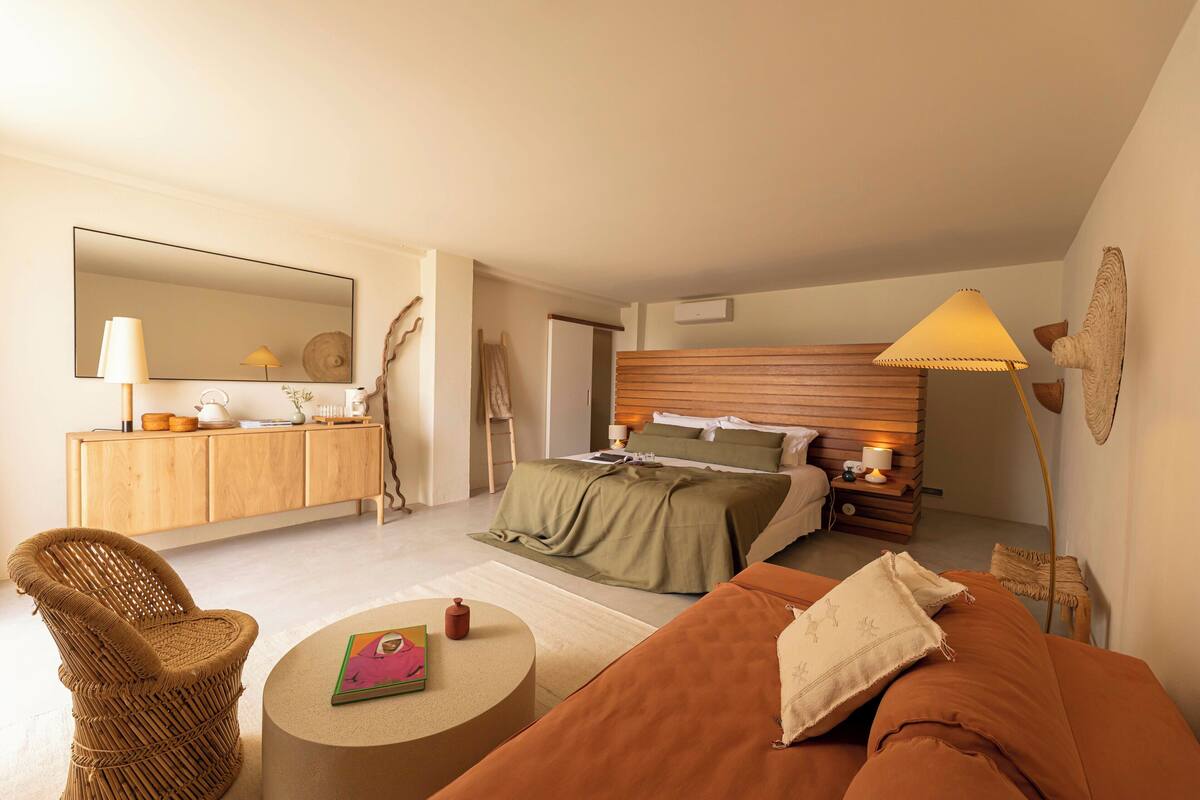 Une chambre à coucher moderne avec un lit, une table de chevet, une lampe et un fauteuil en osier.