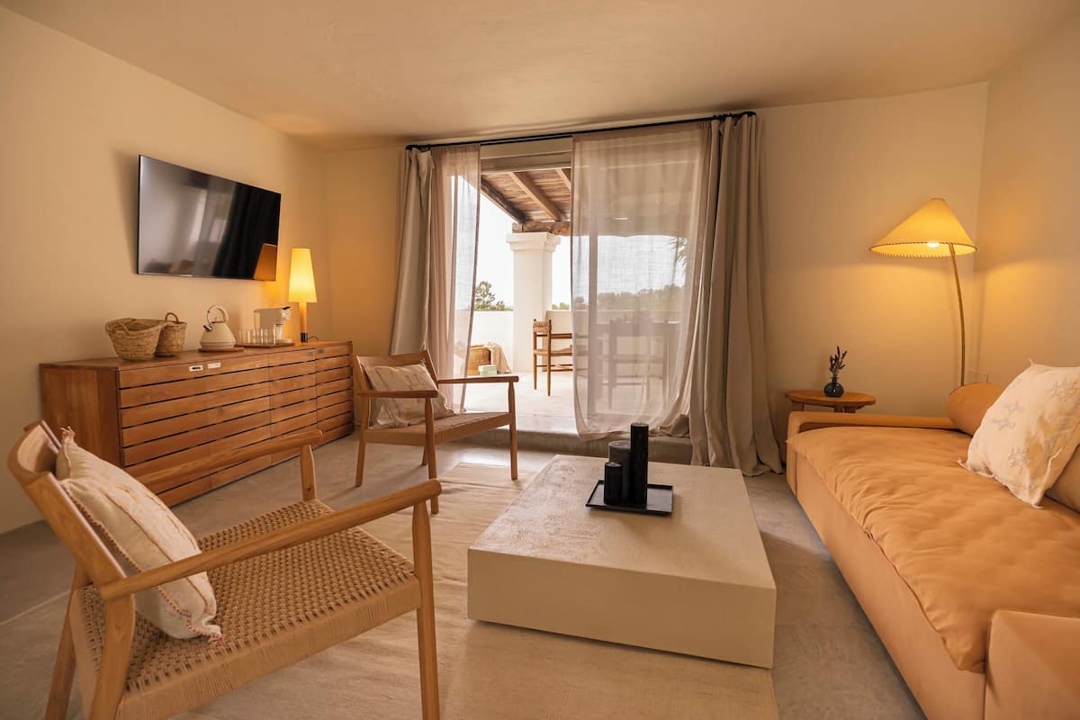 Un salon moderne comprenant un canapé, deux fauteuils, une table basse, un téléviseur et un balcon avec vue.